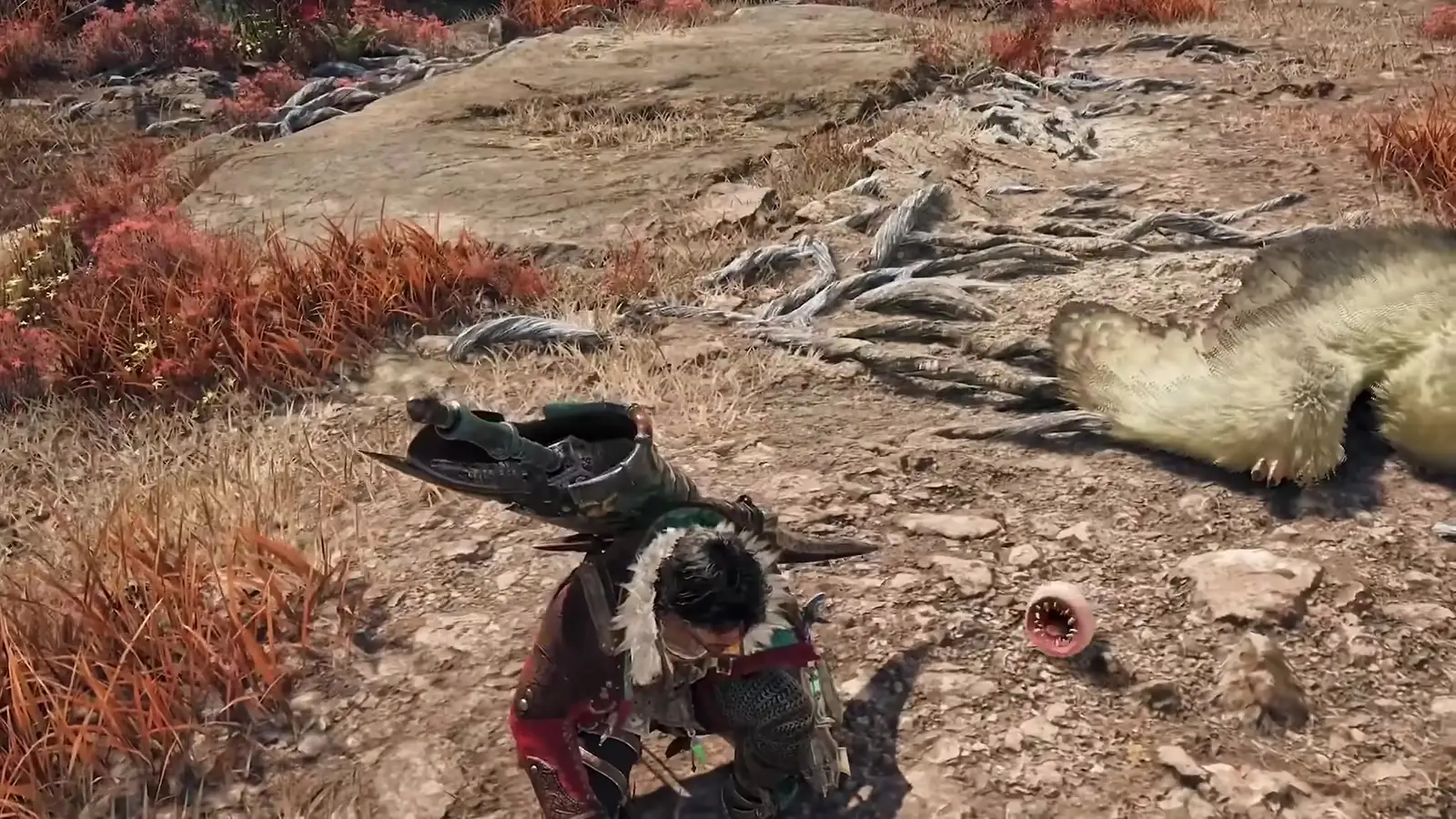 A small pink Khezu whelp with its toothed mouth open on red grass next to a crouching hunter in Monster Hunter Wilds Ascendance